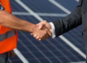 Foreman and businessman shaking hands at solar energy station. Close up view on handshake between worker and man in business suit.
